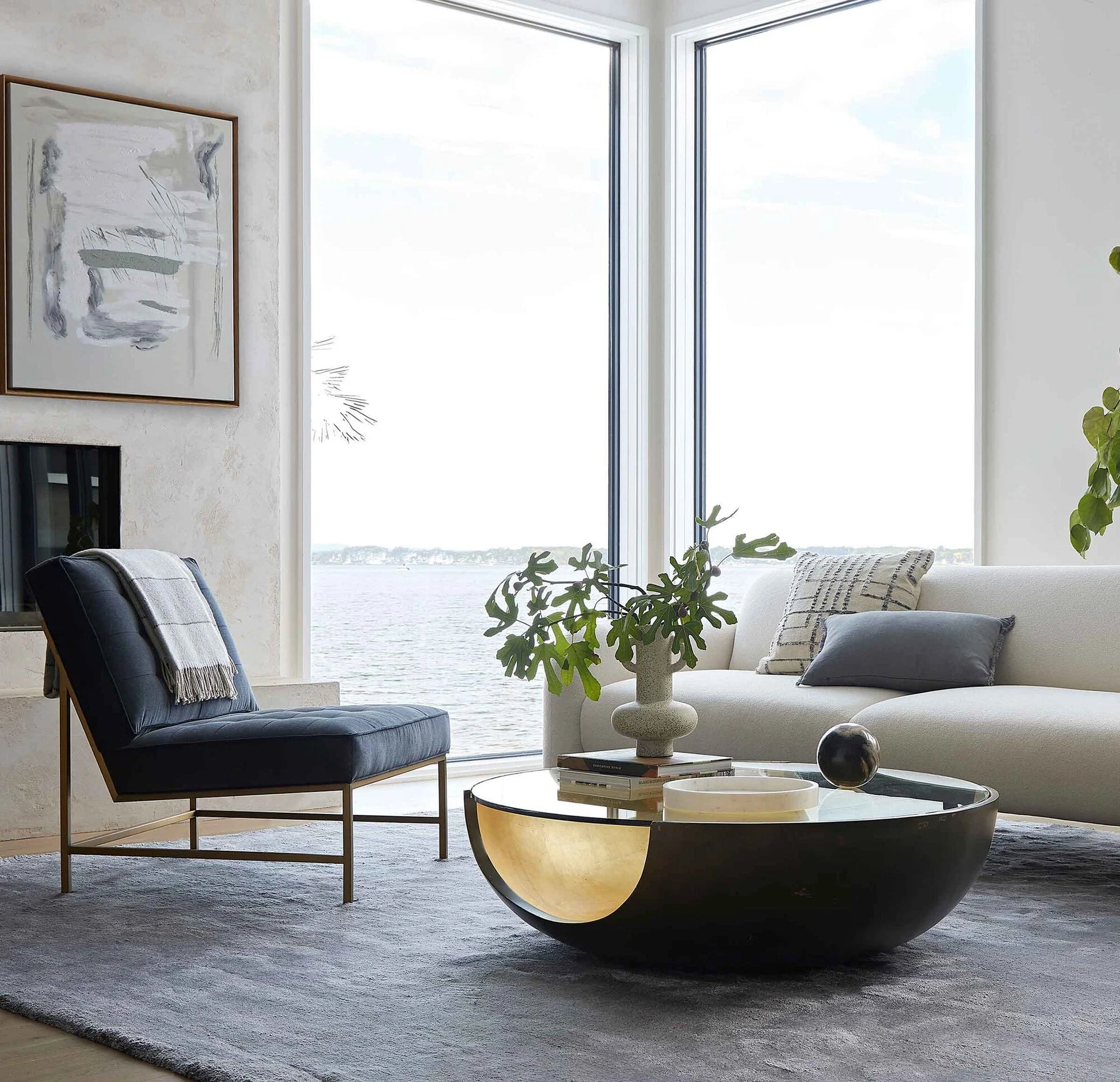 Pictured in this lifestyle photo is the Soleil Cocktail by Modern Elements Furniture in a bronze / gold leaf finish. The Soleil Cocktail, part of the Phoenix Collection, is an American-made resin cocktail table featuring a distinctive cut-out base design, paired with a sleek tempered glass top that enhances its modern appeal. The rounded base showcases a beautiful two-tone finish, adding depth and dimension to its sculptural form.