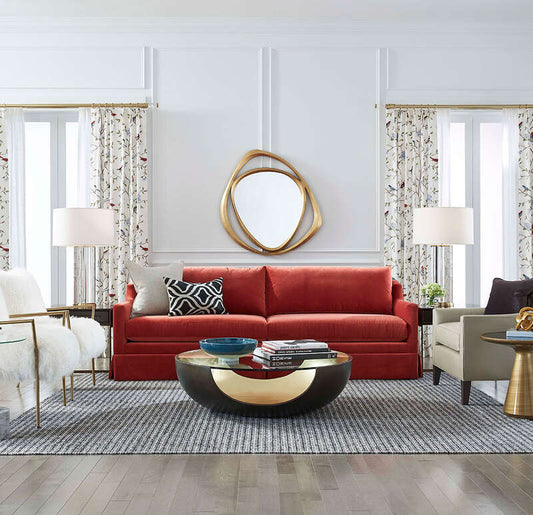 Pictured in this lifestyle photo is the Soleil in a bronze / gold leaf finish. The Soleil Cocktail, part of the Phoenix Collection, is an American-made resin cocktail table featuring a distinctive cut-out base design, paired with a sleek tempered glass top that enhances its modern appeal. The rounded base showcases a beautiful two-tone finish, adding depth and dimension to its sculptural form.