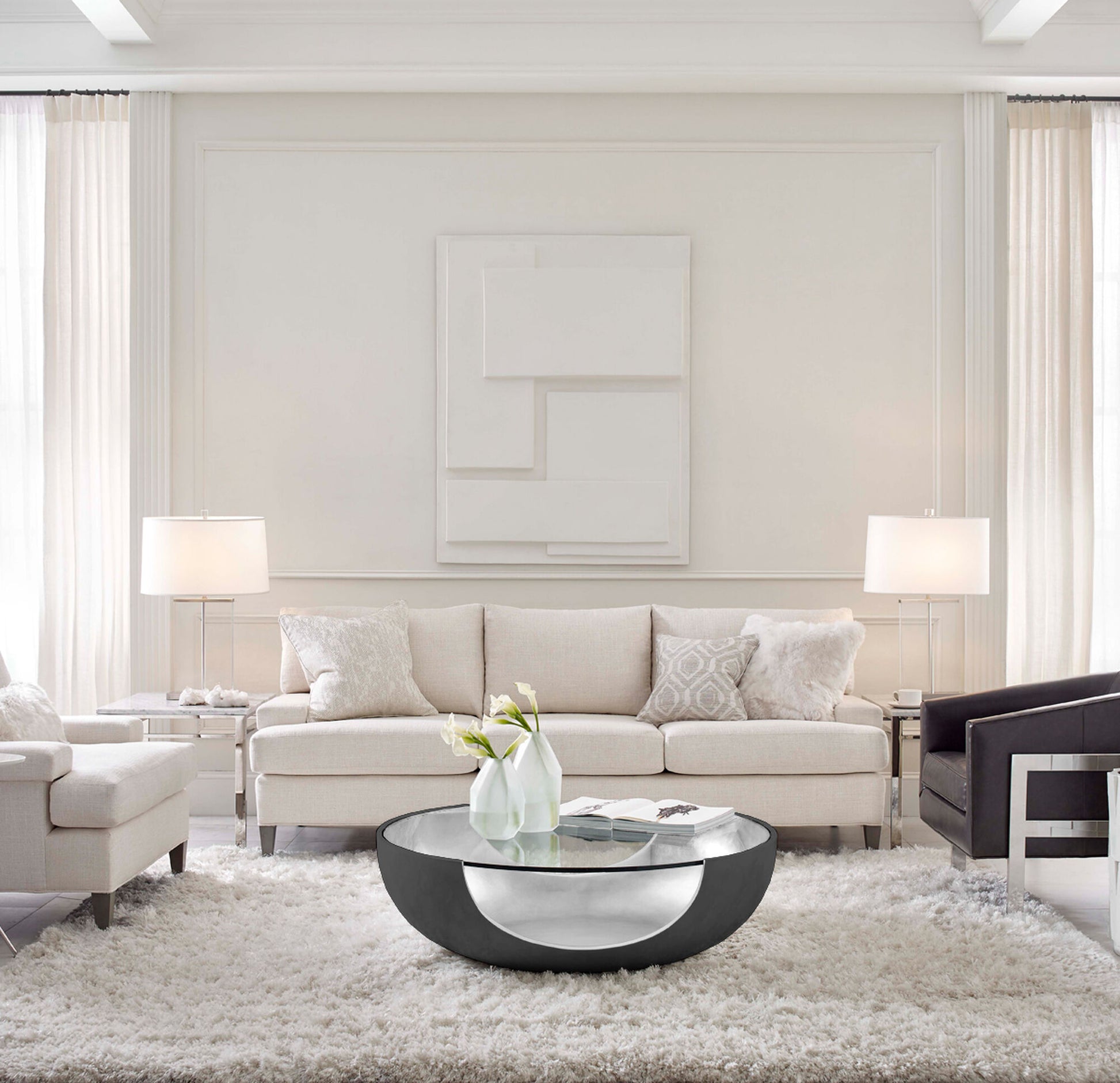 Pictured in this lifestyle photo is the soleil in a Pewter / Silver Leaf finish. The Soleil Cocktail, part of the Phoenix Collection, is an American-made resin cocktail table featuring a distinctive cut-out base design, paired with a sleek tempered glass top that enhances its modern appeal. The rounded base showcases a beautiful two-tone finish, adding depth and dimension to its sculptural form.