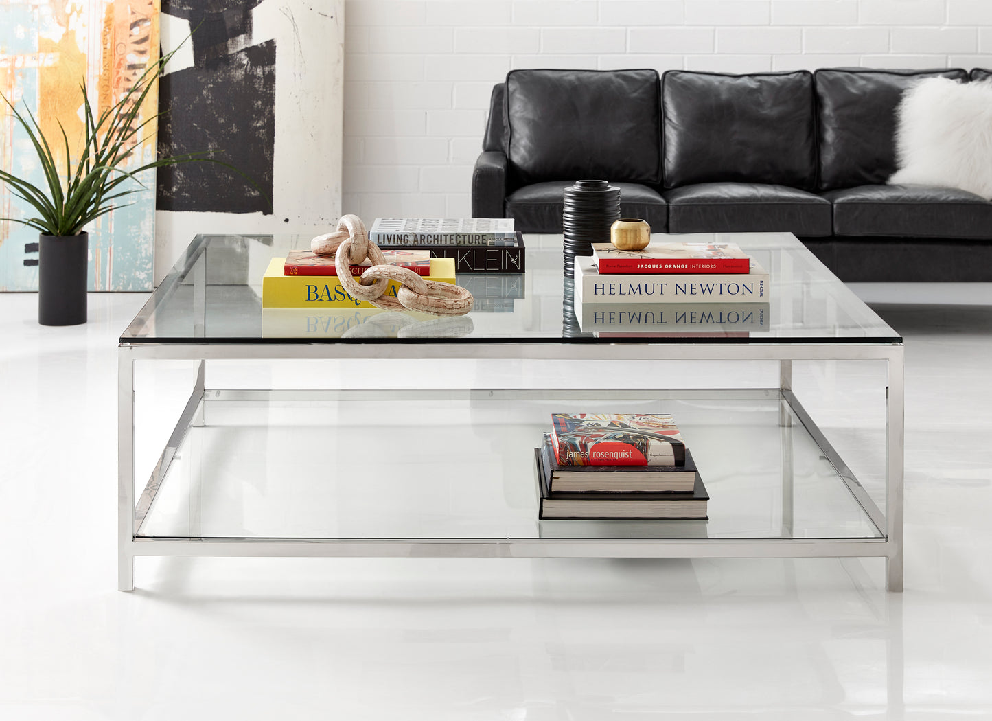 This is a lifestyle shot of the square Basis Cocktail table by Modern Elements. Like its counterpart, the Basis Rectangular, this square cocktail is crafted with metal and glass, showcasing the clean lines of its simple yet outspoken design.