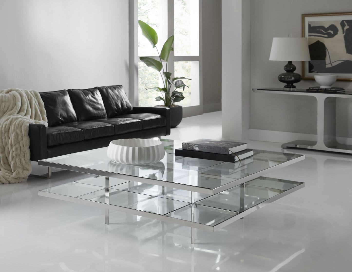 In this lifestyle photo, The Romo Cocktail Table is a perfect blend of modern design and timeless elegance, making it an ideal centerpiece for any contemporary living space.
Available in two sizes—54" x 54" x 18" and 60" x 60" x 18"—this square cocktail table features a sleek metal base paired with a clear glass top that exudes sophistication and style. Its minimalist lines and balanced proportions make it a versatile choice for both large and small living rooms.