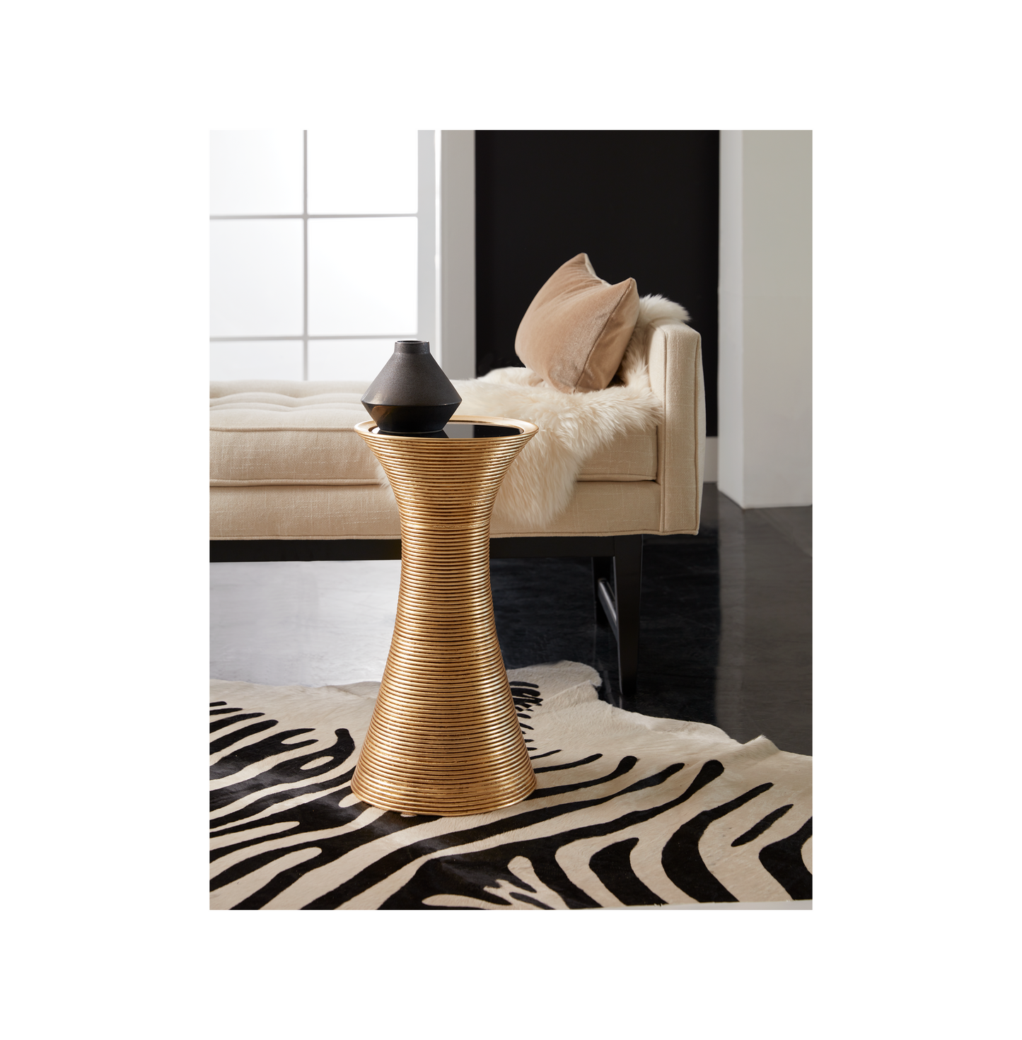 This is a lifestyle shot of the Cota by Modern Elements placed in a contemporary living room, shown here in a gold leaf finish with a black glass insert.