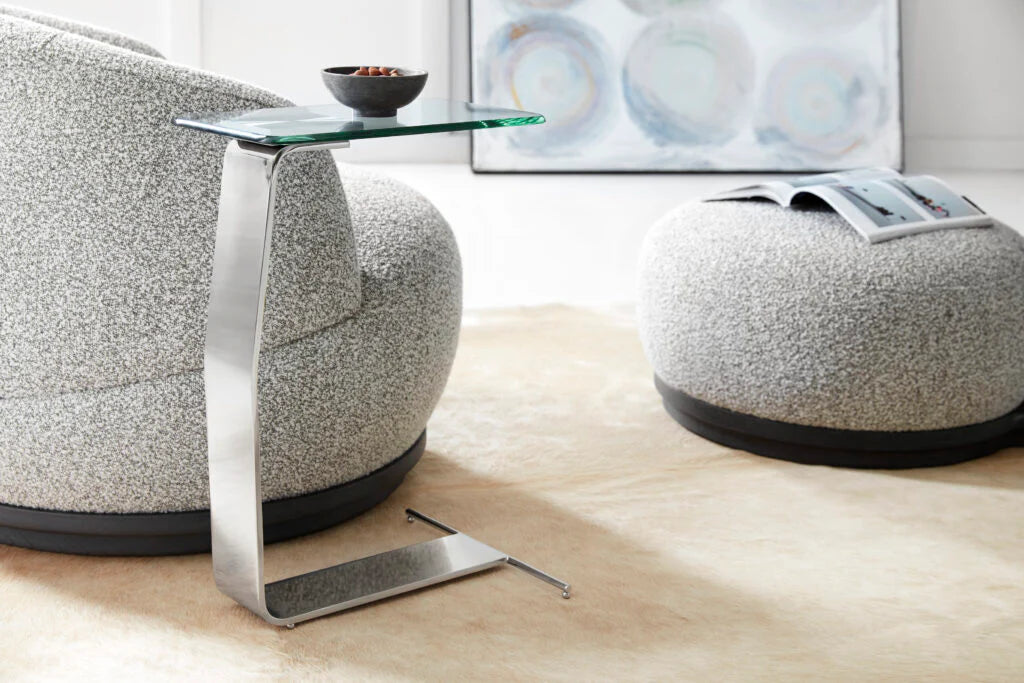 This is a lifestyle photo of the Plateau Side table shown in brushed stainless.

Featuring a clear glass tabletop that rests on a sleek, sculptural metal frame, this metal and glass side table adds a touch of sophistication to your home decor. The unique frame, crafted from a single piece of metal, creates a contemporary sculpture-like form that serves as both a functional end table and a stylish accent piece.
