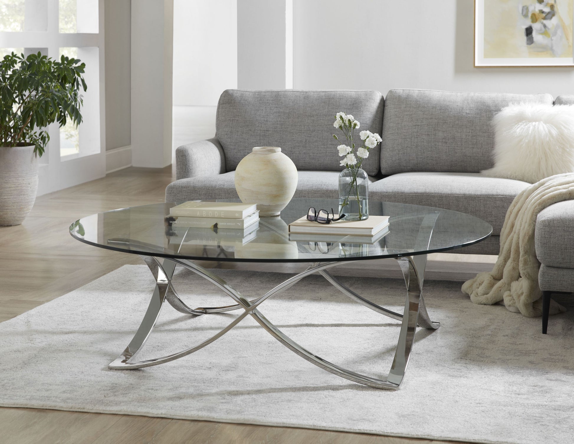 This is a lifestyle shot of the Diana Cocktail table, showcasing its unique table base and classic glass table top.