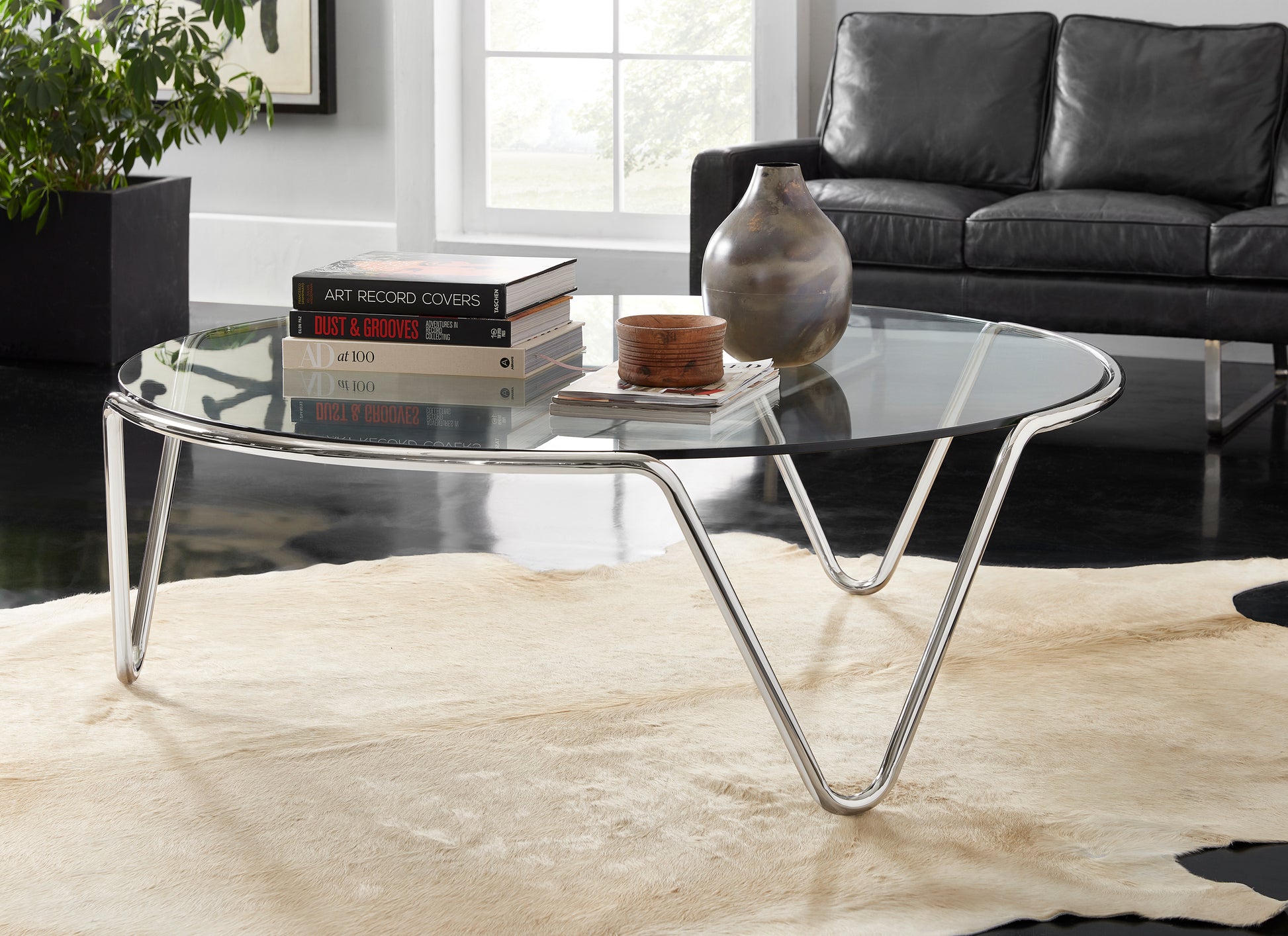 Pictured in this lifestyle shot, The Ripple Cocktail Table is a modern masterpiece that brings an artistic touch to any living room or lounge area.

Featuring a round glass top and a sleek metal frame, this contemporary cocktail table offers a sophisticated and airy look that complements a variety of decor styles. The table's subtle yet refined base design creates a sense of fluidity and elegance, making it a unique statement piece for modern interiors. 