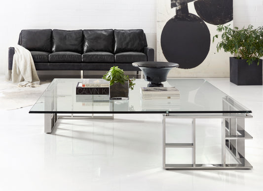 Pictured in this lifestyle photo is the Template Cocktail by Modern Elements Furniture. The Template Cocktail Table is a stunning example of modern design with a futuristic flair, making it a captivating centerpiece for any living room or lounge area.

This square-topped cocktail table features a sleek glass top paired with a stainless steel frame, creating a sophisticated and airy aesthetic. The table’s base showcases a unique geometric design with two 90-degree wrapped corners.