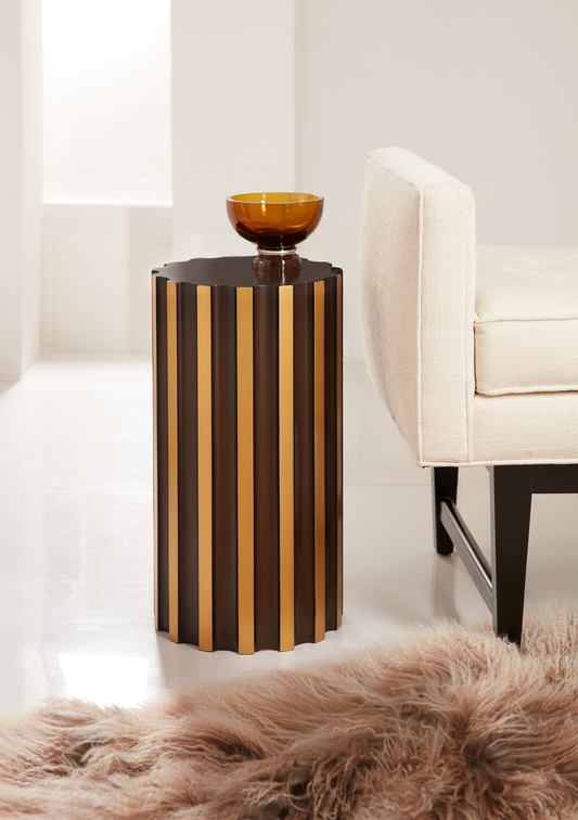 Pictured in this lifestyle photo is the Malla Spot table by Modern Elements. This resin pull-up table draws inspiration from the elegance of Ionic columns, creating an artistic and sculptural element that enhances the decor of any room. Finished in a luxurious Bronze with Gold accents, The Malla adds a touch of bold sophistication to both contemporary and traditional settings. 