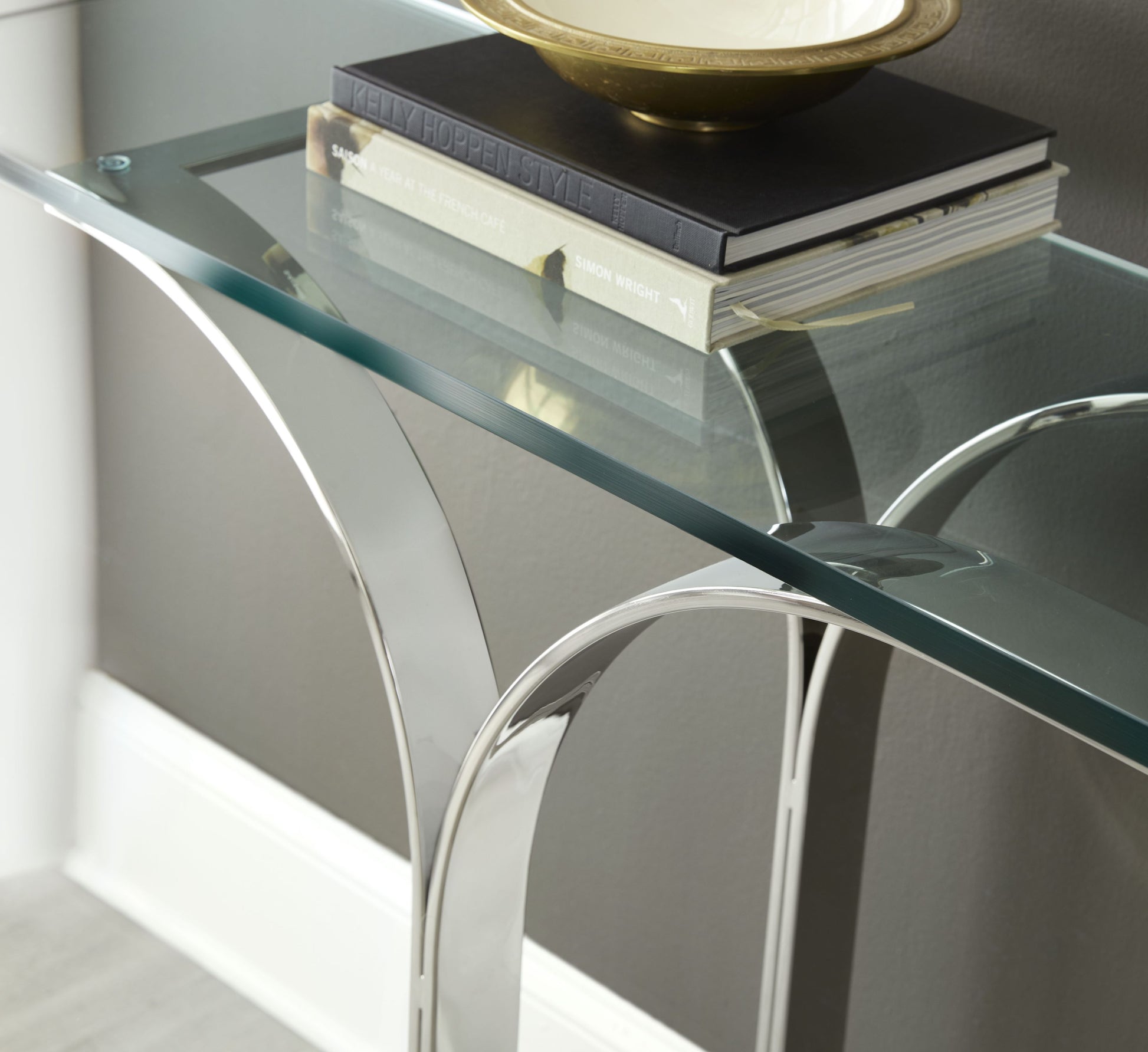 Pictured here in this detail shot, The Trellis Console Table is a sleek and sophisticated addition to any lounge area or living room. Featuring a sturdy stainless steel base and a clear glass tabletop, this console table embodies a modern aesthetic with its clean lines and minimalist form.

Inspired by the intricate geometric patterns of a classic trellis design, the table’s base showcases an elegant interplay of lines and angles, creating a visually striking effect.