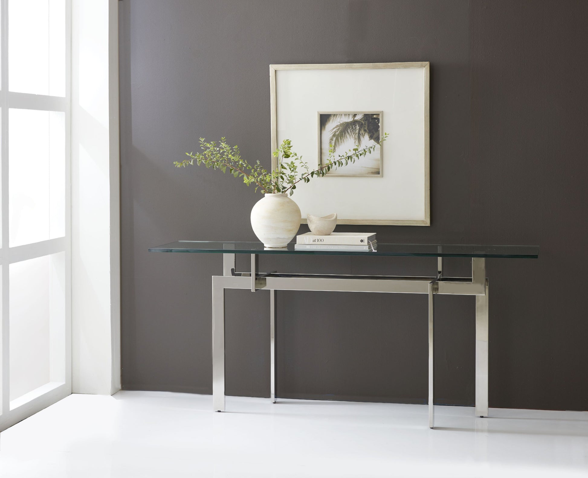 Crafted with a stainless steel frame and a clear glass tabletop, The Zig Zag Console Table features an intricate base design where the table legs create an optical illusion, appearing to zig-zag as they connect to the tabletop. Its unique contemporary geometric design adds visual interest and makes it a true statement piece for any space.